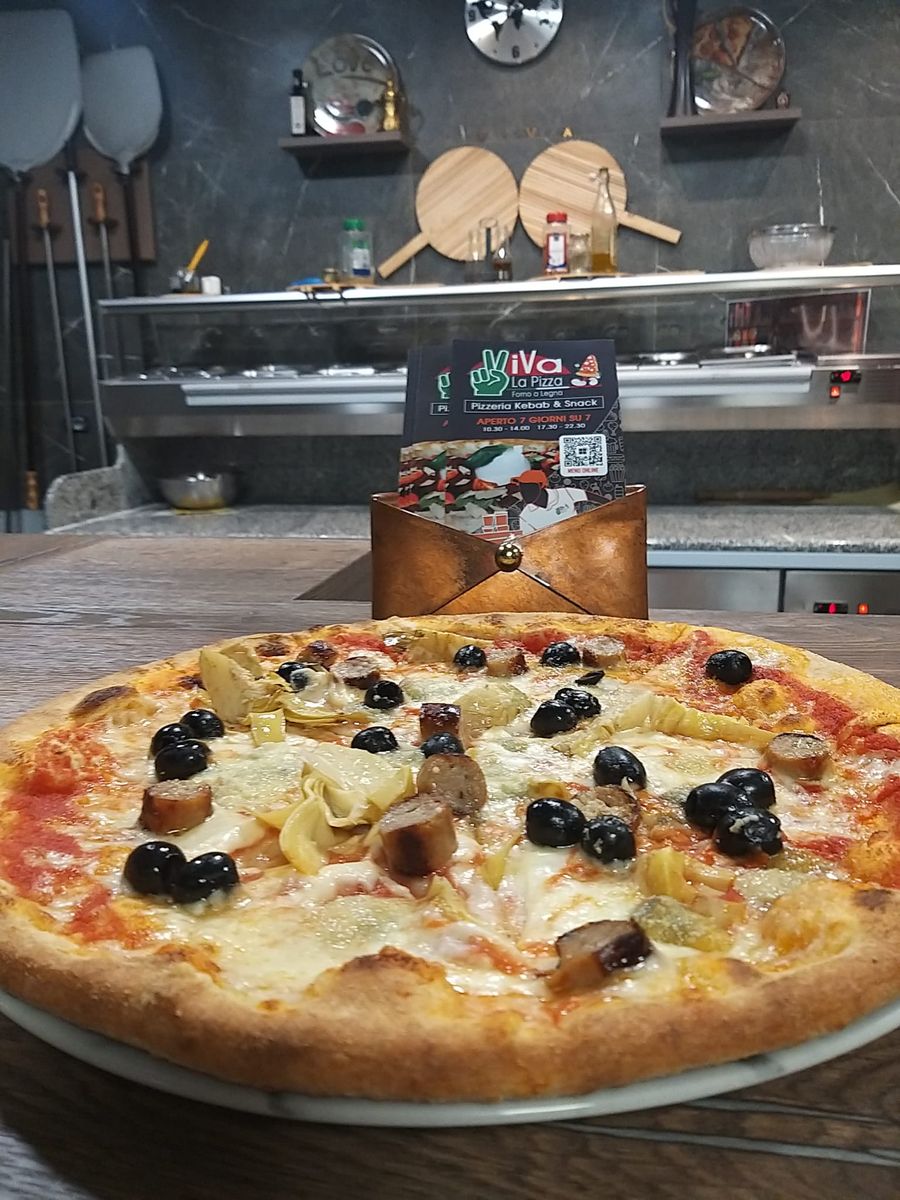 Il bancone del locale con il volantino della pizzeria e una pizza con olive, carciofi e funghi.