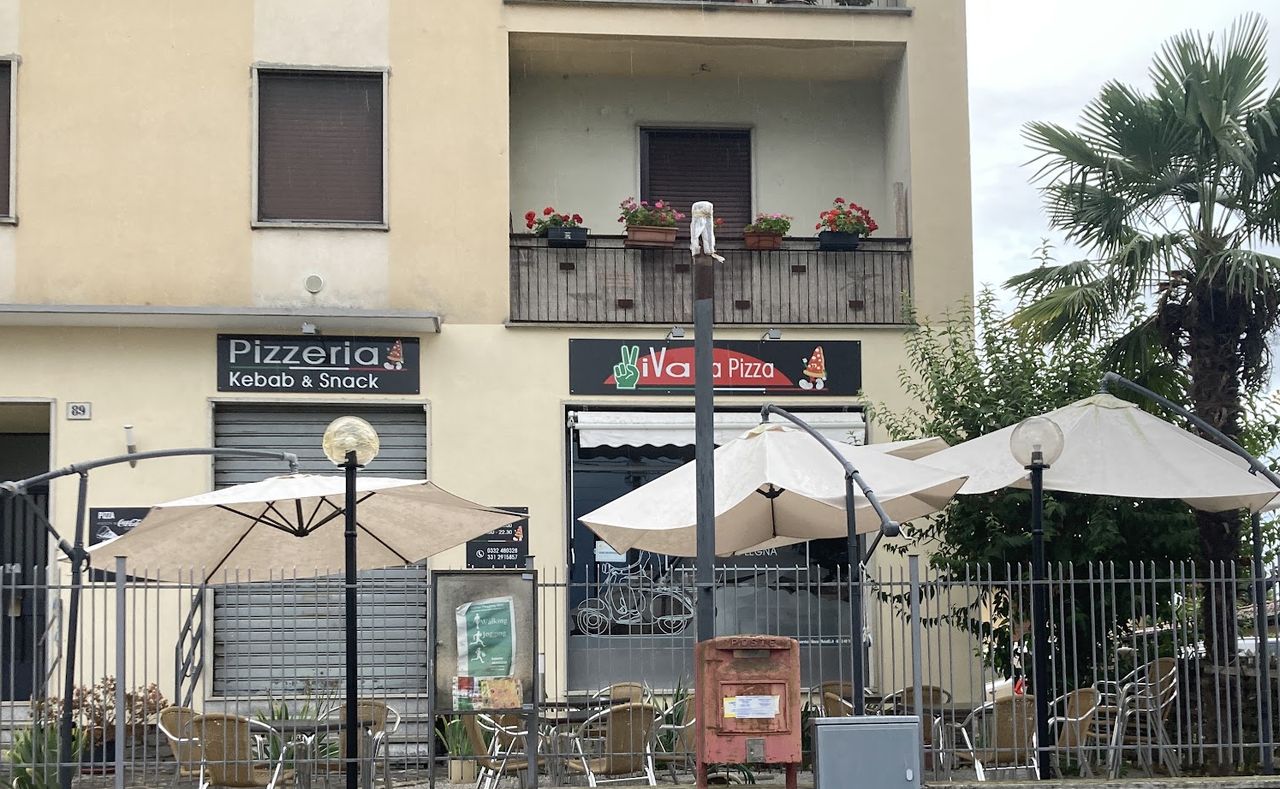 L'esterno del locale: le insegne Pizzeria Kebab & Snack e ViVa La Pizza sopra la porta, tavoli e ombrelloni davanti.
