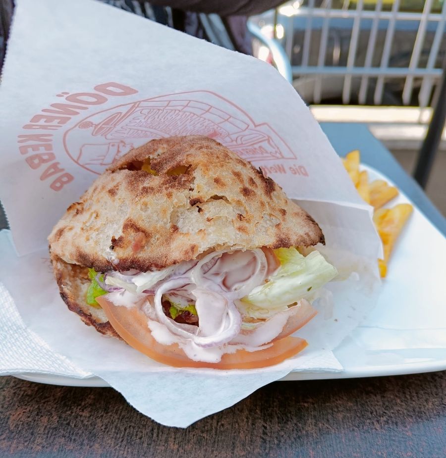 Panino con kebab, cipolla, insalata e pomodoro, servito su carta.