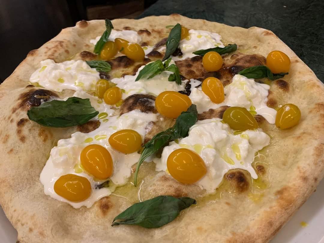 Pizza appena sfornata con stracciatella, datterini gialli e foglie di basilico.