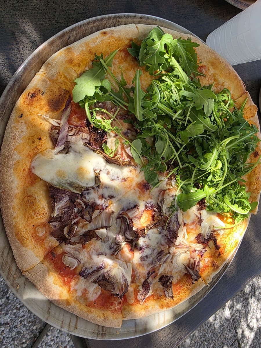 Pizza con radicchio e un ciuffo di rucola fresca, su un piatto di metallo.